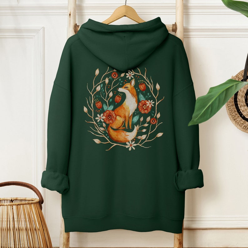 May include: A dark green hooded sweatshirt with a graphic print of a fox sitting in a circle of flowers and branches. The fox is orange and white, and the flowers are red, orange, and white.