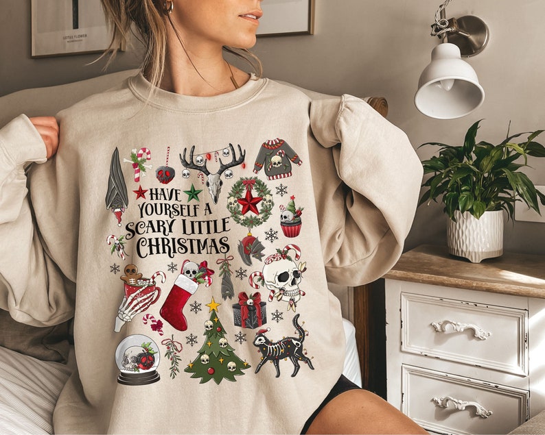 May include: A beige sweatshirt with a festive Christmas design featuring skulls, candy canes, and the text "Have Yourself a Scary Little Christmas".
