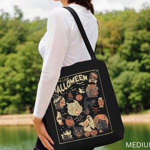 May include: A black tote bag with a vintage-style illustration of Halloween characters. The bag features a black cat, a ghost, a witch, and pumpkins. The text "Going Live Halloween" is printed on the bag.