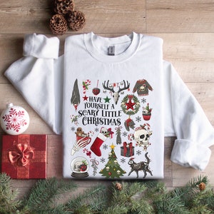 May include: White sweatshirt with a festive, spooky Christmas design. The design features skulls, candy canes, a Christmas tree, a stocking, and the text "Have Yourself a Scary Little Christmas".