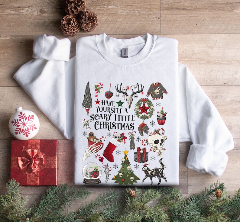May include: White sweatshirt with a festive, spooky Christmas design. The design features skulls, candy canes, a Christmas tree, a stocking, and the text "Have Yourself a Scary Little Christmas".