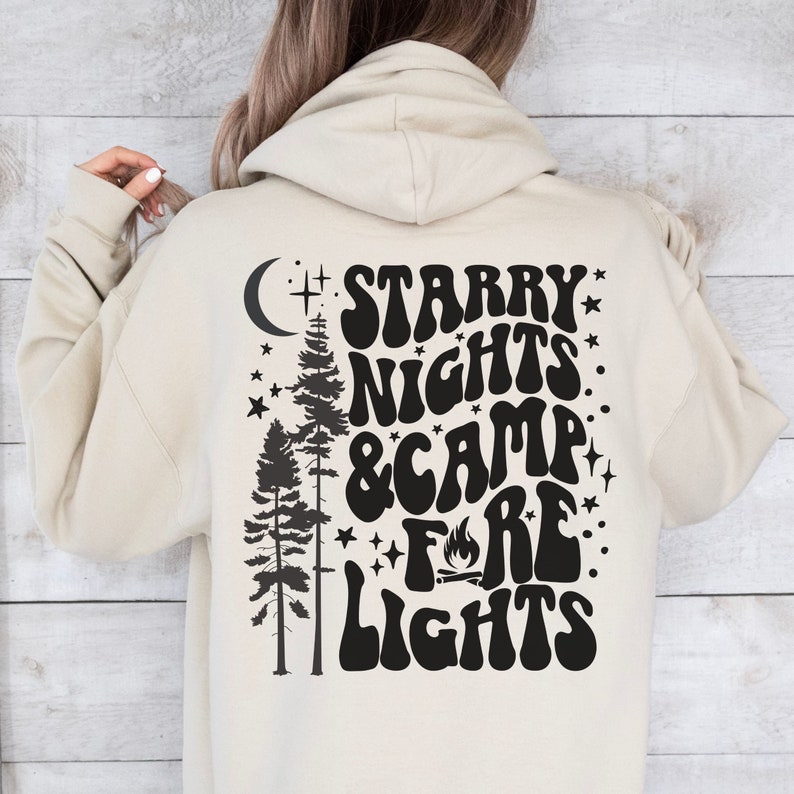 May include: A beige hoodie with a black graphic print that says "Starry Nights & Camp Fire Lights" with a crescent moon, stars, and pine trees.