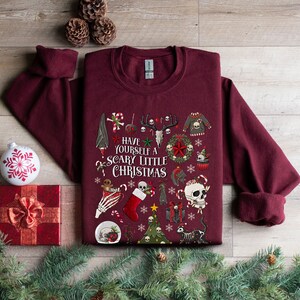 May include: A maroon sweatshirt with a festive Christmas design featuring skulls, bats, candy canes, and the text "Have Yourself a Scary Little Christmas".