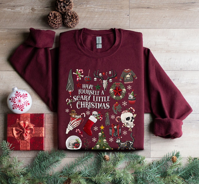 May include: A maroon sweatshirt with a festive Christmas design featuring skulls, bats, candy canes, and the text "Have Yourself a Scary Little Christmas".