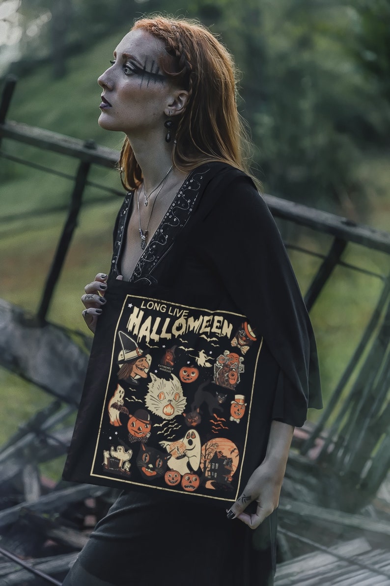 May include: A woman wearing a black dress and a tote bag with a vintage Halloween illustration. The bag features a white cat, pumpkins, ghosts, and the text "Long Live Halloweeen".