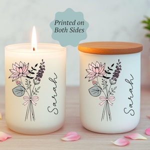 May include: Two white candles with floral designs and the name "Sarah" printed on them. One candle is lit, and the other has a wooden lid. The floral design includes pink lotus flowers, purple sprigs, and green leaves. The text "Printed on Both Sides" is also visible.