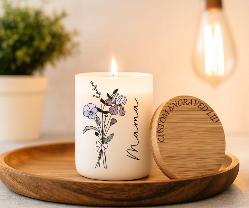 May include: A lit white candle with a floral design and the word "Mama" in script. The candle sits on a wooden tray with a matching lid that reads "CUSTOM ENGRAVED LID". The candle features purple and lavender flowers.