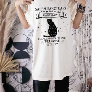 Może przedstawiać: Biały t-shirt z grafiką czarnego kota i tekstem "Salem Sanctuary for Wayward Cats. Feral and Familiars Welcome. Est. 1692."