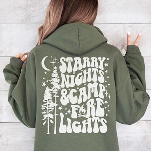 May include: A green hooded sweatshirt with a white graphic print on the back that says "Starry Nights & Camp Fire Lights" with a crescent moon, stars, and pine trees.