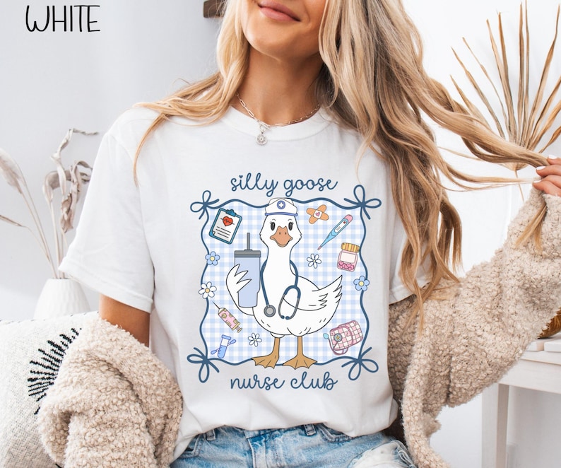 May include: White t-shirt with a cartoon goose wearing a nurse's hat and stethoscope, surrounded by medical-themed illustrations. The text "silly goose nurse club" is displayed above and below the goose. The word "WHITE" is in the upper left corner.