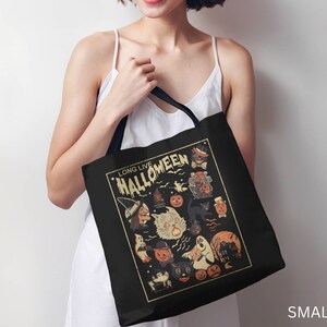 May include: A black tote bag with a white design featuring a vintage Halloween illustration. The design includes a witch, a cat, a ghost, and pumpkins. The text "Long Live Halloweeen" is printed in a vintage font.