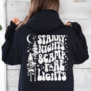 May include: Black hooded sweatshirt with a white graphic print of a moon, stars, trees, and the text "Starry Nights & Camp Fire Lights".