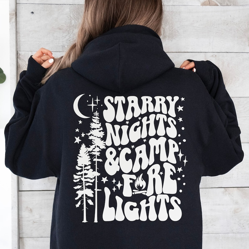 May include: Black hooded sweatshirt with a white graphic print of a moon, stars, trees, and the text "Starry Nights & Camp Fire Lights".