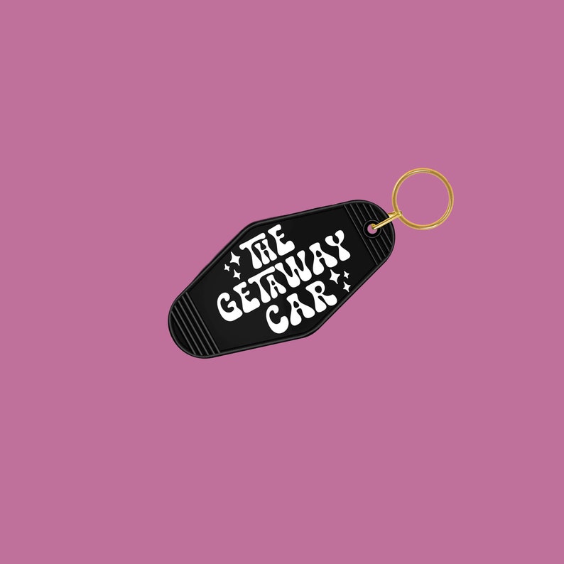 Black keychain against a dark pink background, featuring the phrase The Getaway Car surrounded by white vinyl star designs.