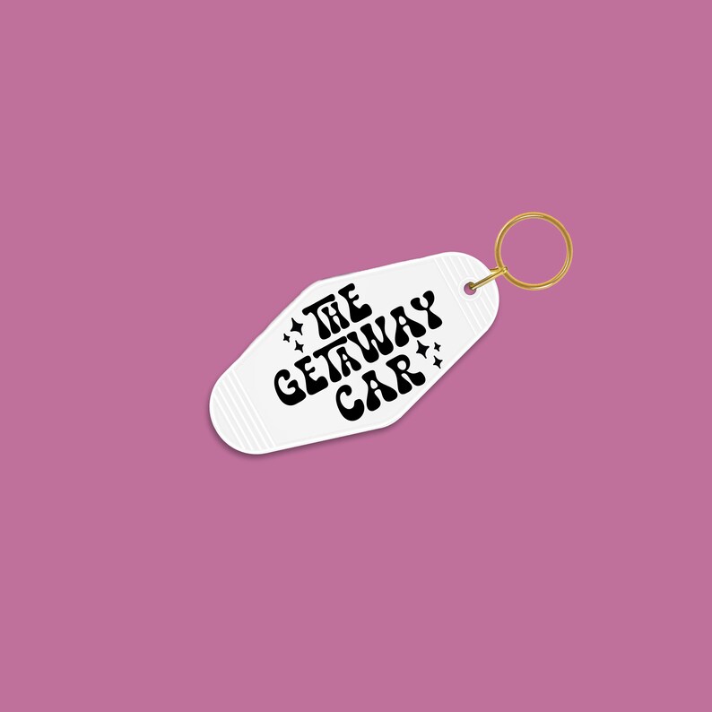 White keychain against a dark pink background, featuring the phrase The Getaway Car surrounded by black vinyl star designs.