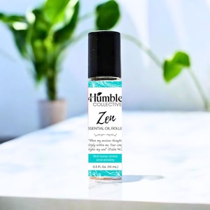 May include: A small essential oil roller bottle with a black cap and a label that reads "Humble Collective Zen." The label is white and teal with the text "Roll away stress and anxiety." The bottle contains 10 ml.