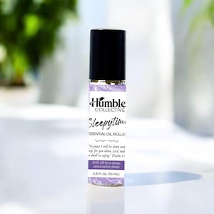 May include: A small essential oil roller bottle with a black cap and a label featuring the text "Sleepytim" and "Humble Collective." The label includes a Bible verse and states the bottle contains 0.3 fl oz (10 mL) of oil.