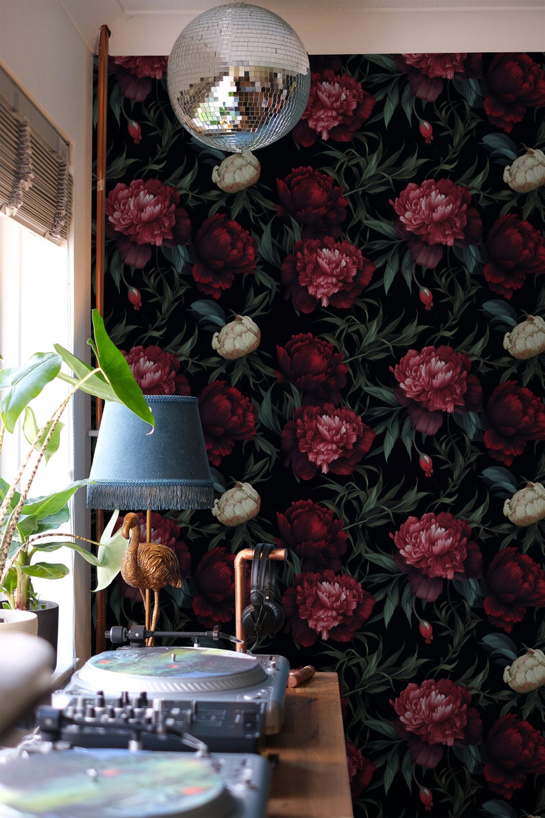 May include: A black and green floral wallpaper with large red and pink peonies. A gold flamingo lamp with a blue lampshade sits on a wooden table with a record player.