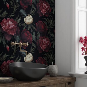 May include: Black and white floral wallpaper with large red and white peonies. A black oval sink with a gold faucet is in the foreground.