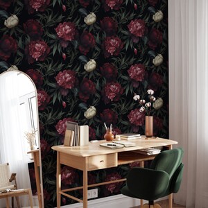 May include: A dark floral wallpaper with a repeating pattern of burgundy and white peonies and green leaves. The wallpaper is shown in a home office setting with a wooden desk, a green chair, and a mirror.