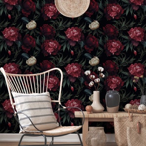 May include: A black and white floral wallpaper with dark red peonies. A wicker chair with a striped cushion sits in front of a wooden table with a woven basket and a vase with white cotton flowers.