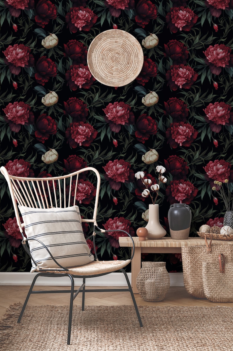 May include: A black and white floral wallpaper with dark red peonies. A wicker chair with a striped cushion sits in front of a wooden table with a woven basket and a vase with white cotton flowers.