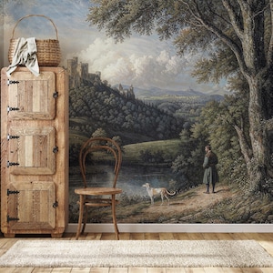 Wooden cabinet and chair against a vintage scenic peel and stick wallpaper, showcasing a wooded medieval castle hillside and tranquil river.