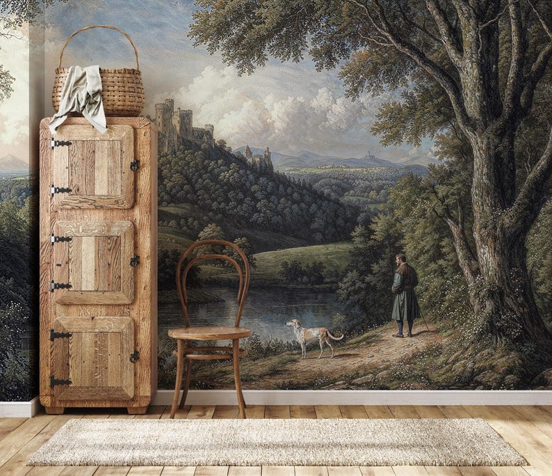 Wooden cabinet and chair against a vintage scenic peel and stick wallpaper, showcasing a wooded medieval castle hillside and tranquil river.