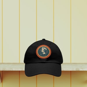 Può includere: Cappellino da baseball nero con una toppa rotonda arancione e blu con un'illustrazione di uno chef.