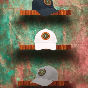 May include: Three baseball caps displayed on wooden shelves against a textured wall. The caps are navy blue, white, and grey. Each cap features a circular patch with a guitar design on the front.