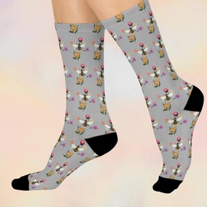 May include: A pair of gray socks with a repeating pattern of bees, flowers, and berries. The socks have black heels and toes. The bees are yellow and black, and the flowers are yellow, pink, and purple.