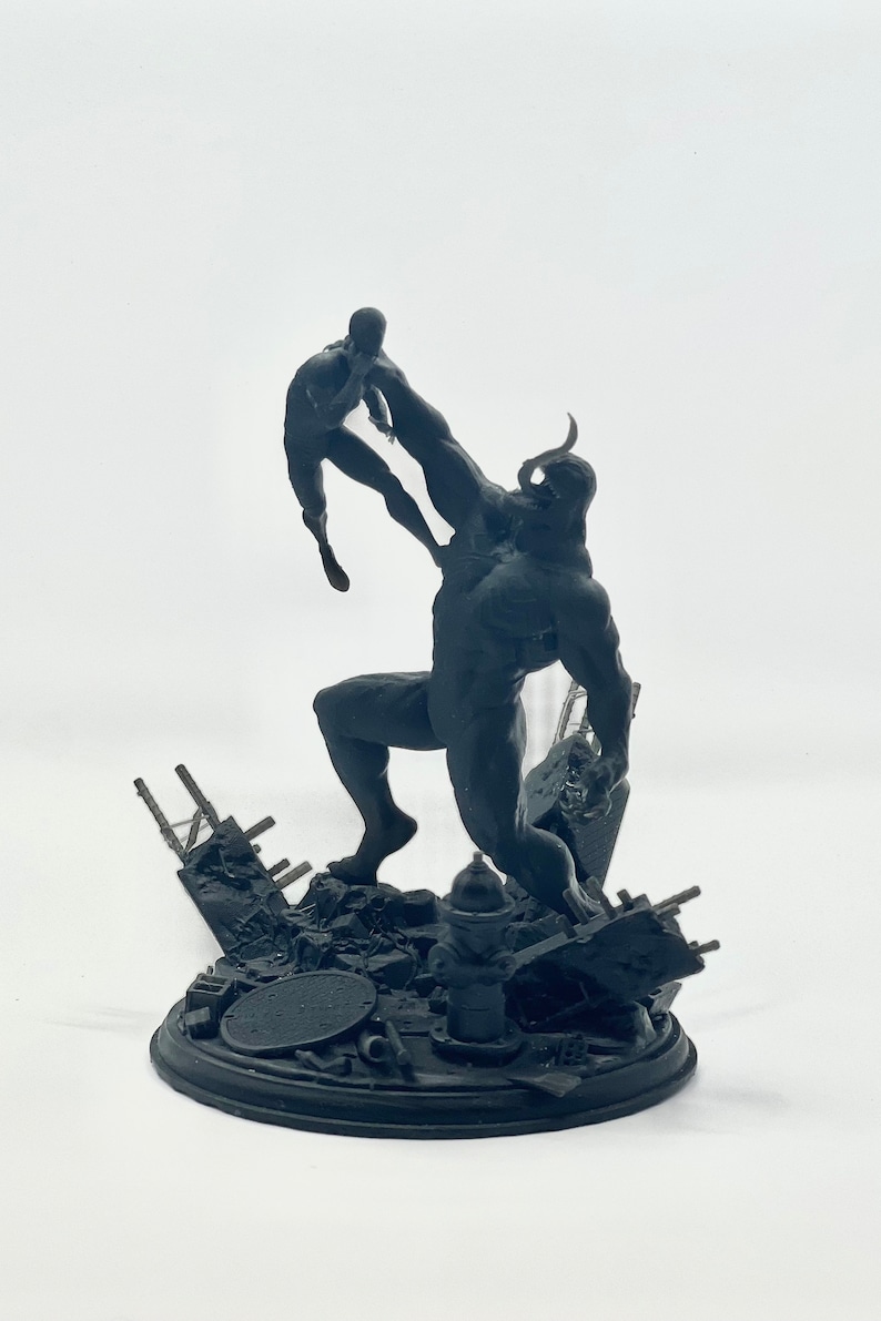 May include: A black and white 3D printed figurine of a large, muscular figure holding a smaller figure in its hand. The larger figure has horns and a menacing expression. The smaller figure is in a fighting pose. The figurine is set on a base with a destroyed cityscape.