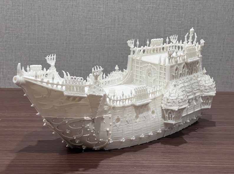 May include: A white, detailed model of a ship with intricate carvings and a gothic design. The ship has a tall, pointed bow and a large, ornate stern.