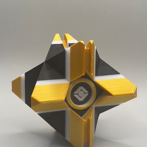 May include: A 3D printed yellow, black, and white ghost with a white and gray symbol in the center.