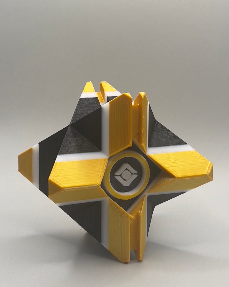 May include: A 3D printed yellow, black, and white ghost with a white and gray symbol in the center.
