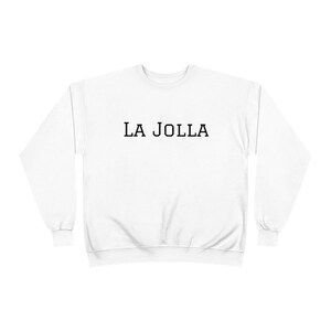May include: White crew neck sweatshirt with the text "LA JOLLA" printed in black, centered on the chest. The sweatshirt has long sleeves and a classic, casual design.