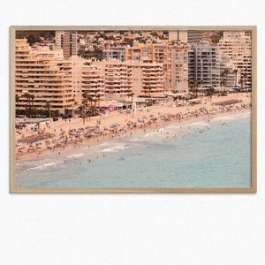 May include: An aerial view of a beach with a large crowd of people on the sand and in the water. The beach is lined with tall, light-colored apartment buildings.