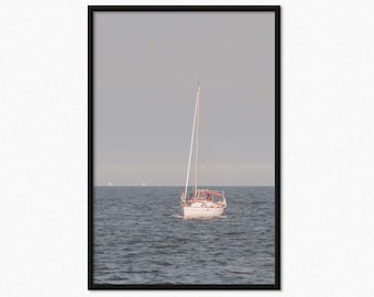 May include: A framed print featuring a white sailboat sailing on a calm sea under a gray sky. The boat has a tall mast and a red awning. The water is a dark blue, and the overall scene evokes a sense of tranquility.