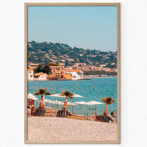 Póster de la playa de la Croisette: pintoresca playa de la Riviera Francesa, vibrante vista al mar con sombrillas, palmeras y decoración de pueblo costero