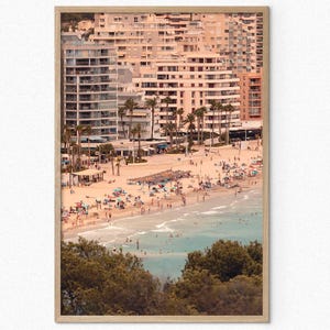 May include: A photograph of a beach scene with a large apartment building in the background. The beach is crowded with people and there are palm trees in the foreground.