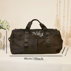 May include: A black duffel bag with the name Nika embroidered in white script. The bag features two top handles, a front pocket, and dimensions of 18 inches in length, 10.2 inches in height, and 7.8 inches in depth as indicated by the text.