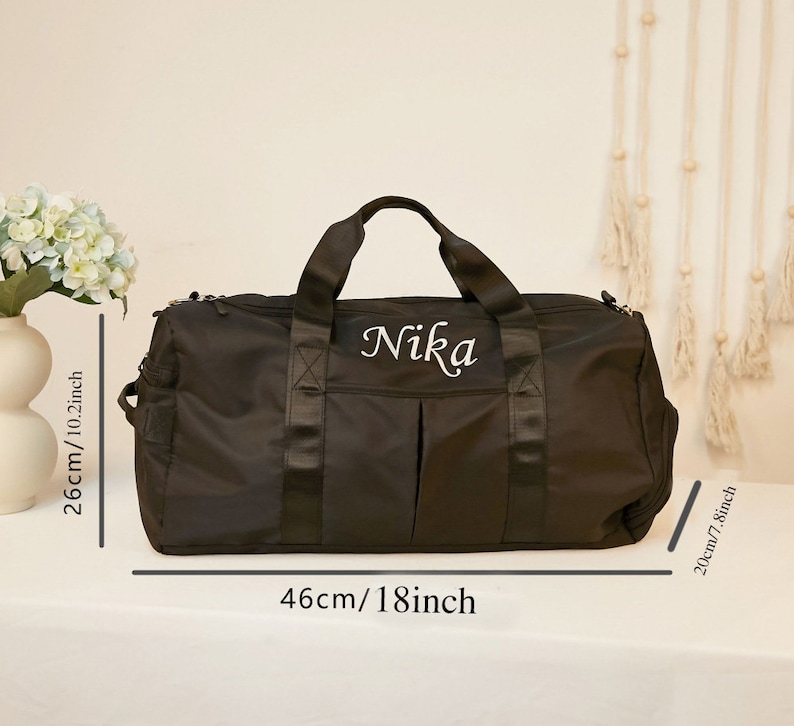 May include: A black duffel bag with the name Nika embroidered in white script. The bag features two top handles, a front pocket, and dimensions of 18 inches in length, 10.2 inches in height, and 7.8 inches in depth as indicated by the text.