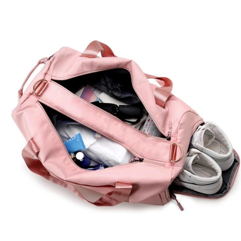 May include: A pink duffel bag with multiple compartments, including a separate shoe compartment. The bag is open, revealing various items inside, such as toiletries and a small umbrella. White sneakers are visible in the shoe compartment.