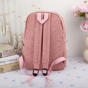 May include: A pink corduroy backpack with adjustable straps and a zipper closure. The backpack has a simple design and is perfect for everyday use.