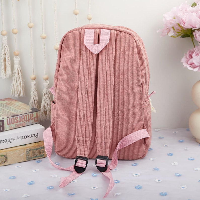 May include: A pink corduroy backpack with adjustable straps and a zipper closure. The backpack has a simple design and is perfect for everyday use.