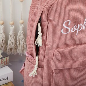 May include: A pink corduroy backpack with a white zipper and a white embroidered name "Sophia".