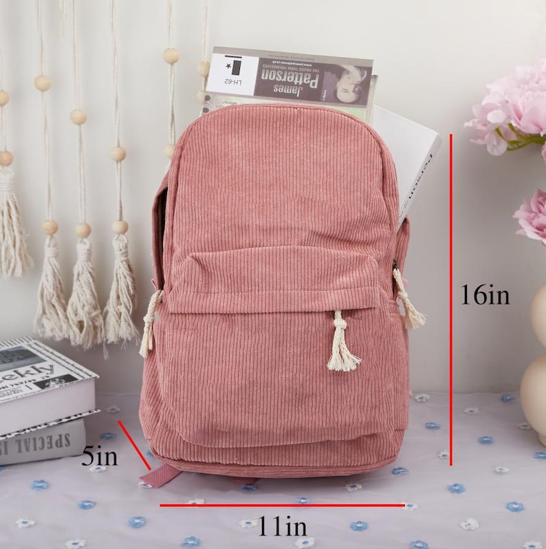 May include: A pink corduroy backpack with a front pocket and white tassel zipper pulls. The backpack measures 11 inches wide, 16 inches tall, and 5 inches deep.