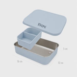 Könnte beinhalten: Eine hellblaue, rechteckige Brotdose mit passendem Deckel, auf dem der Name RALPH steht. Der Behälter enthält einen herausnehmbaren Innenteiler. Die Maße betragen 16 cm mal 12 cm mal 5 cm. Das Innere besteht aus rostfreiem Edelstahl.
