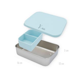 May include: A light blue lunch box with a matching lid and a removable divider. The lid has the name "Kai" in cursive. The stainless steel container is 6.3 inches long, 4.7 inches wide, and 2 inches tall.