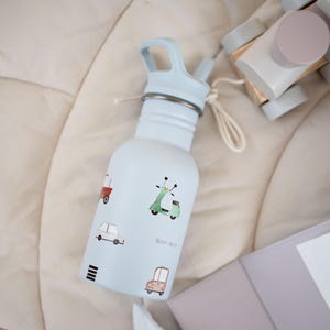 May include: A light blue water bottle with a matching blue lid and straw. The bottle is decorated with small illustrations of vehicles, including a scooter and a car. The text "BEEP-BEEP" is printed on the bottle. A white string is attached to the bottle.